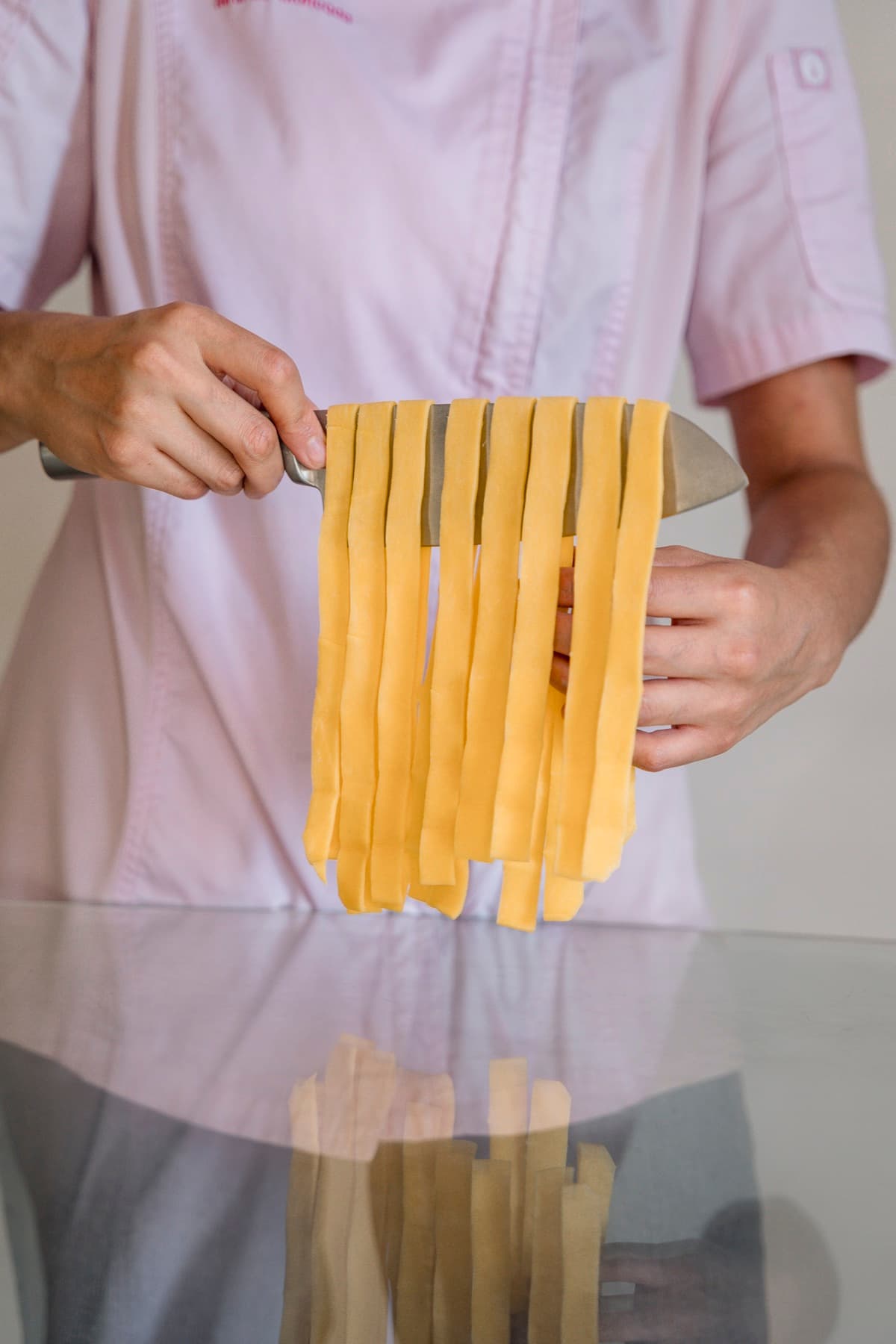 Miranda cortando tiras de pasta fresca con un cuchillo sobre una mesa de cristal